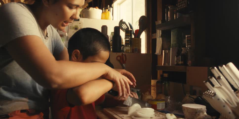 Woman helping a young boy chop onions in a cozy kitchen