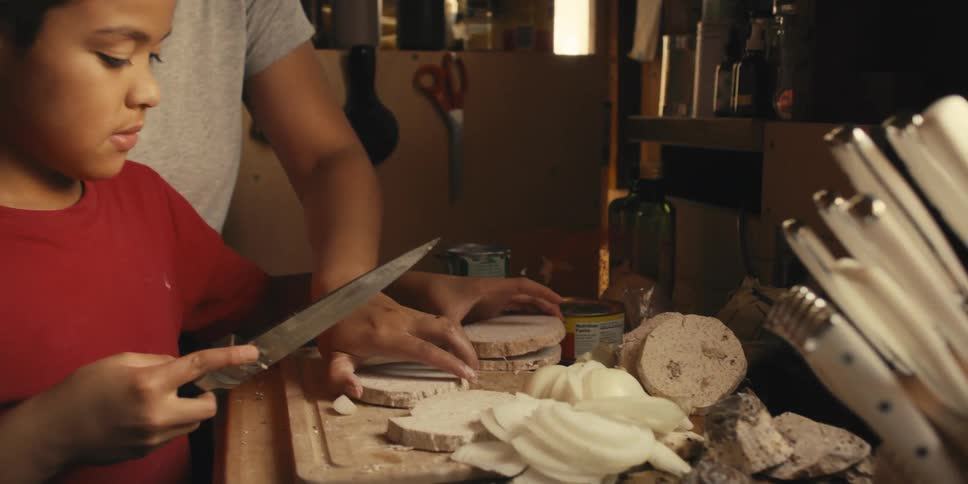 Boy with a knife cutting a vegetable with the help of his mother in the kitchen
