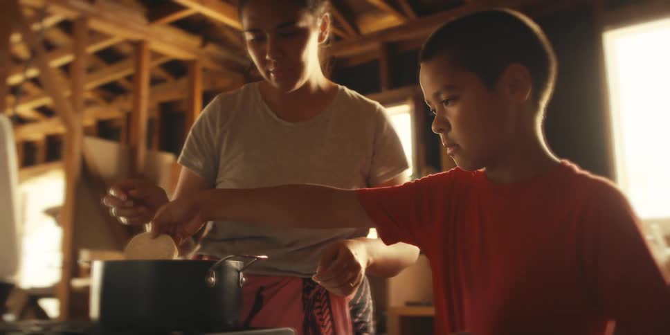 Boy in the kitchen helping his mother cook by putting food in the pan