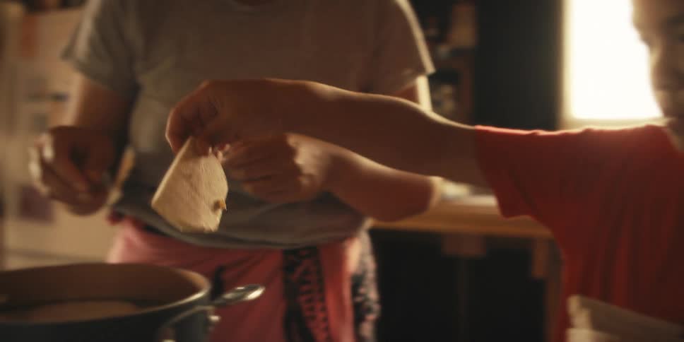 A young boy putting slices of food into a pan that is boiling