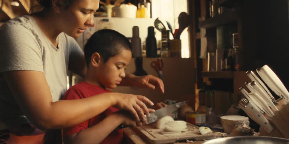 Mother and son with hands together on a knife cutting a vegetable