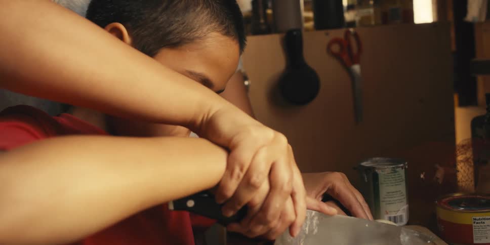 Mother holding her sons hand who is holding a knife and teaching him how to cut an onion
