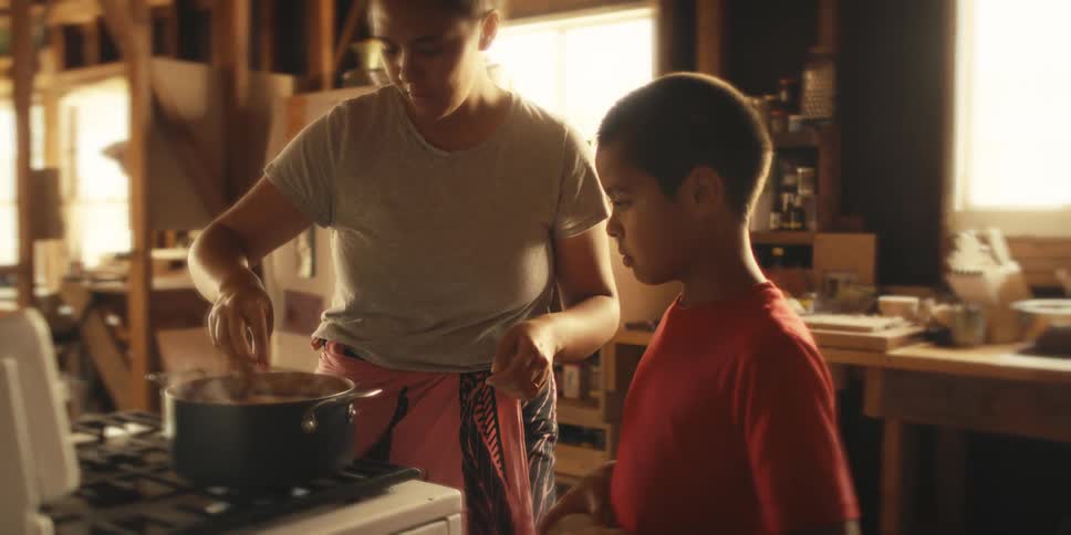 Boy with his mother in the kitchen handing her slices of a vegetable and putting it to cook