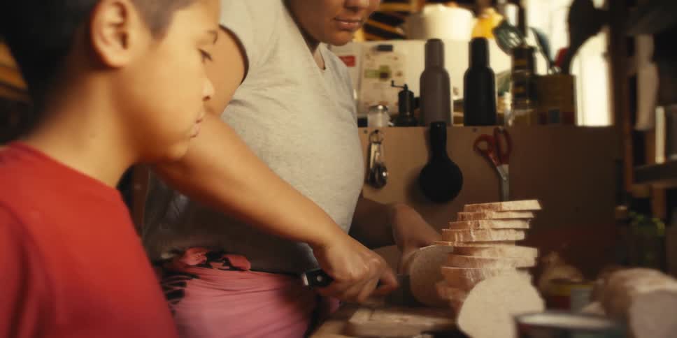 Son watching his mother cut slices of a vegetable