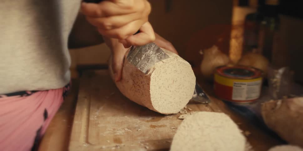 A woman uses a large knife to cut slices of a large root on a cutting board