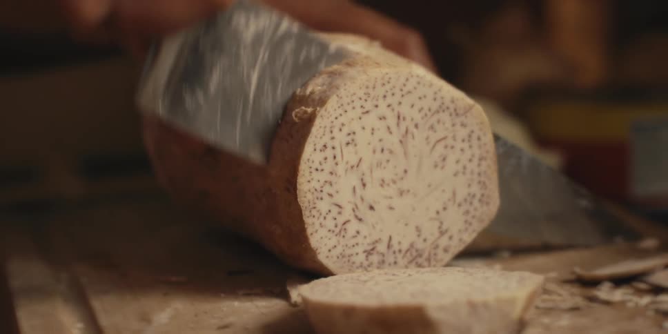 Hand holding a knife and cutting a vegetable on top of a wooden board