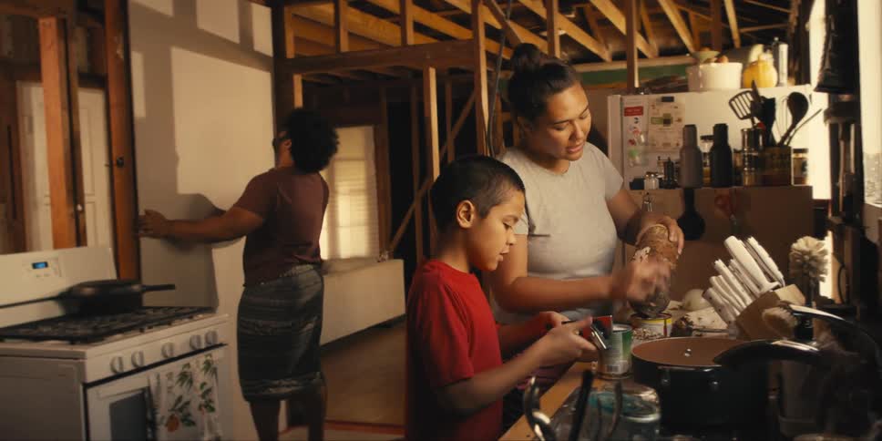 Boy helping his mother in the kitchen and in the background his father positioning a sheet of drywall