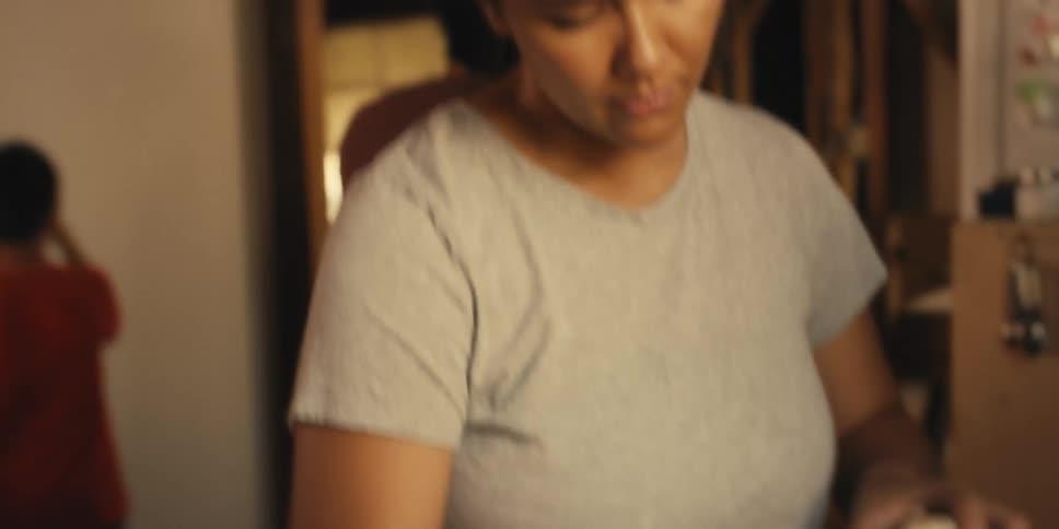 Mother in the kitchen preparing and peeling food and in the background a son with his father using a hammer on the wall