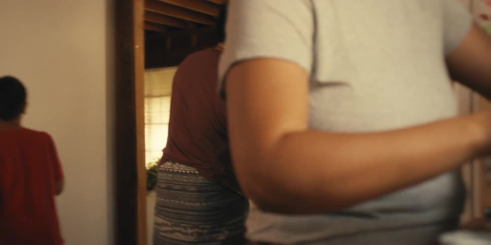 Woman peels a root in the kitchen while her husband hammers a nail into the wall in the background