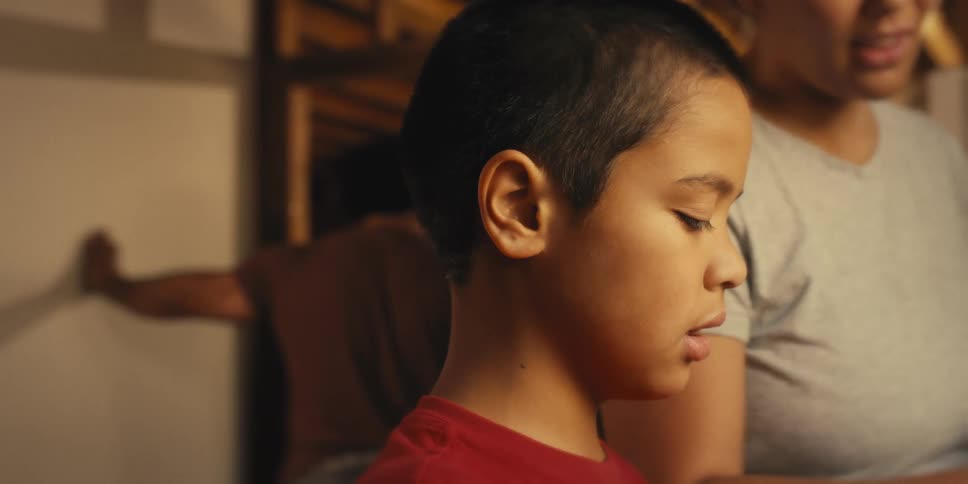 Young boy talking to his mother and in the background his father using a hammer with an irritated expression