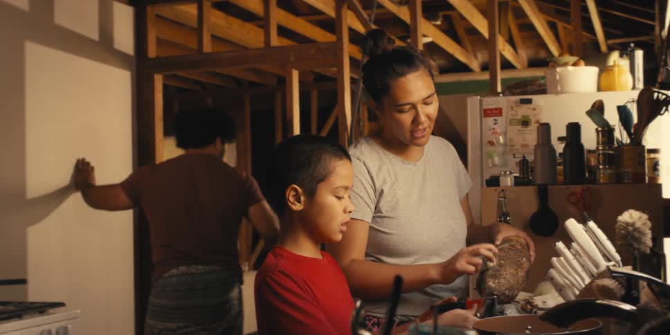 Son helping his mother in the kitchen and his father moving drywall into place and grabs a hammer