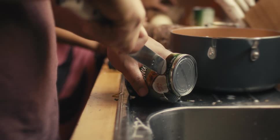 A woman and boy watch a man cut through a can with a knife