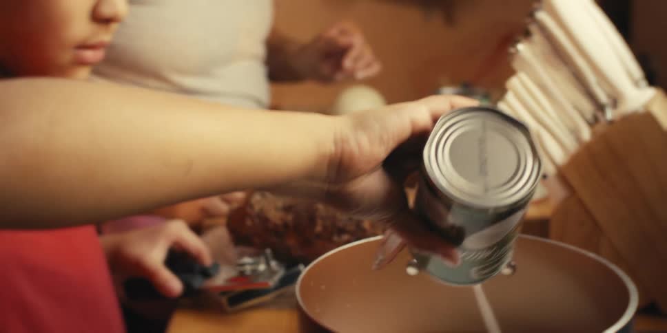 Boy next to his mother preparing food and pouring coconut milk into the pan