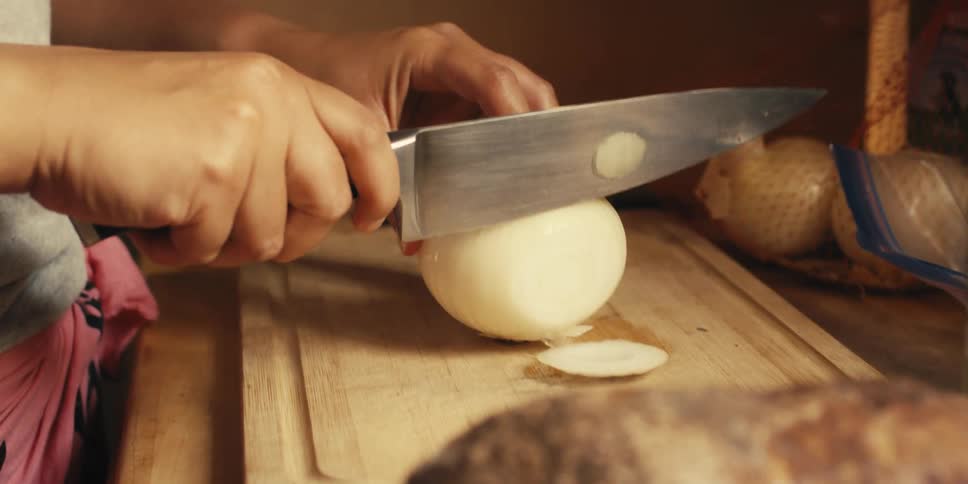Woman uses a knife to slice an onion on a chopping board