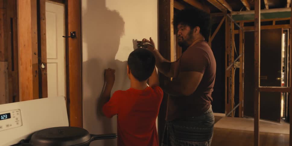 A man and a boy working together to hammer a nail into a wall in a construction setting