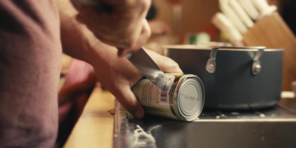 Hands holding a knife and opening a canned food and a child in the background watching