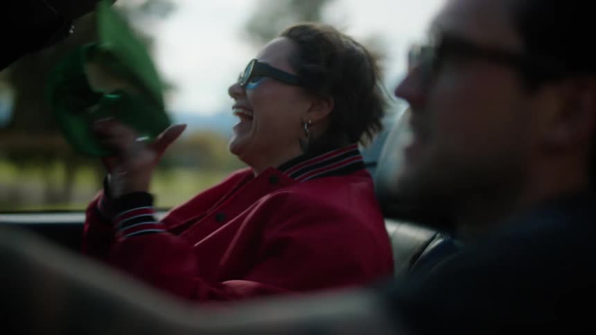 Woman laughing as her green baseball cap flies off while riding in a convertible