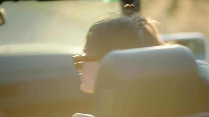 The back of a persons head who is sitting in a convertible car and his hair is flying