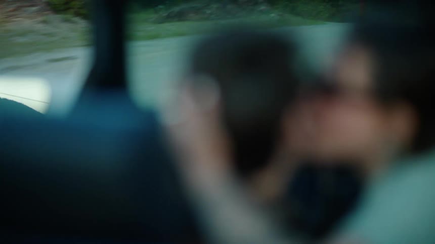 Car in motion and a woman kissing a man who is driving on the cheek