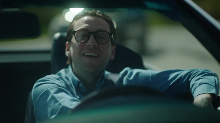 Man with glasses and a smile enjoying a drive in his car hands relaxed on the wheel