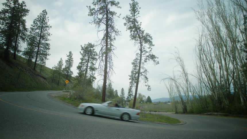 Convertible car making a turn in a natural location with trees around