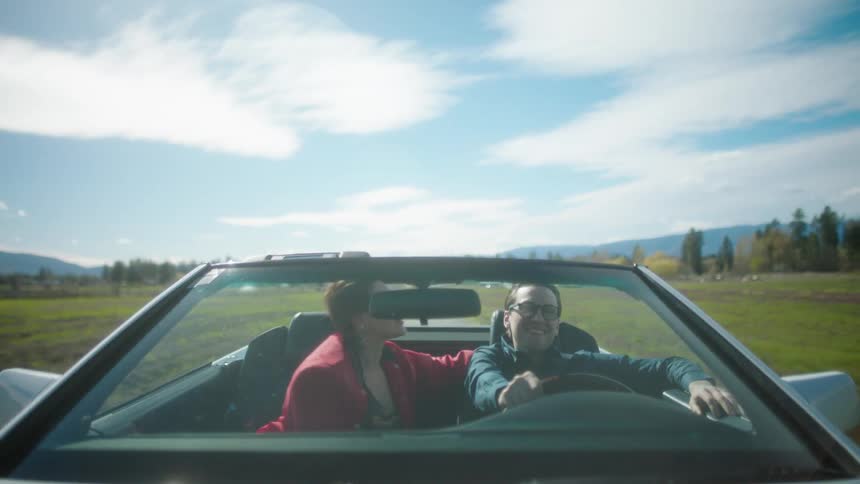 Front of a convertible car in motion and a couple kissing