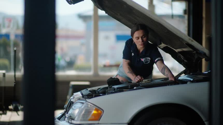 Woman working under the open hood of a car