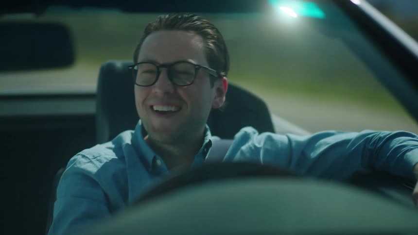 Man smiles while driving his convertible with the top down on a sunny day