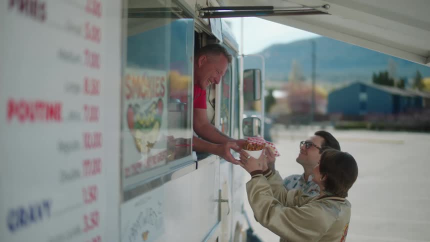 Couple smiles at food truck operator while accepting their food order as traffic passes in the background