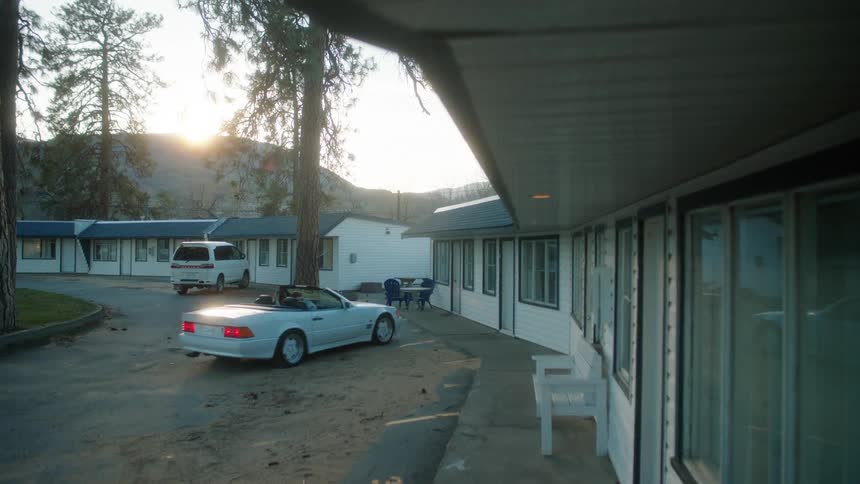 White convertible vehicle with two people inside comparing next to a hotel