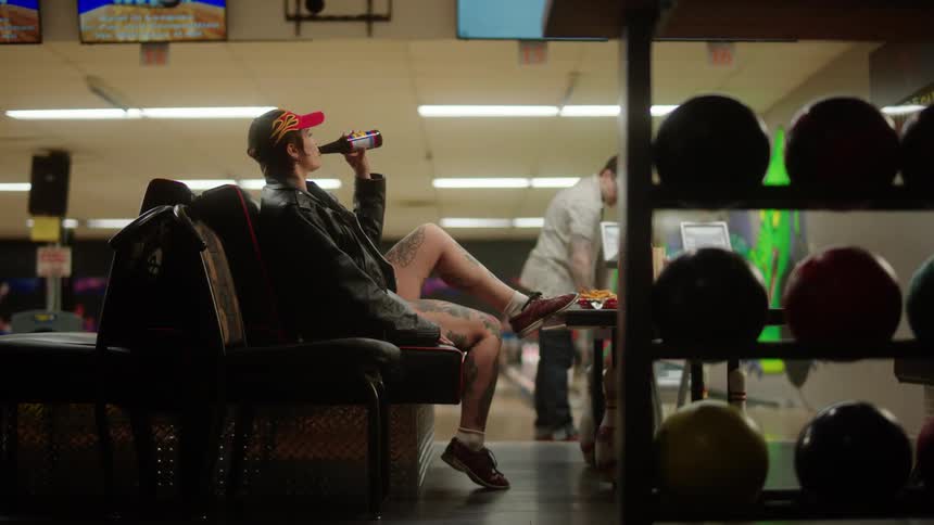 Woman sitting drinking a beer in a bowling alley environment