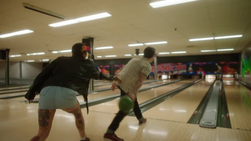 Woman tugs on shirt as her male friend releases the bowling ball