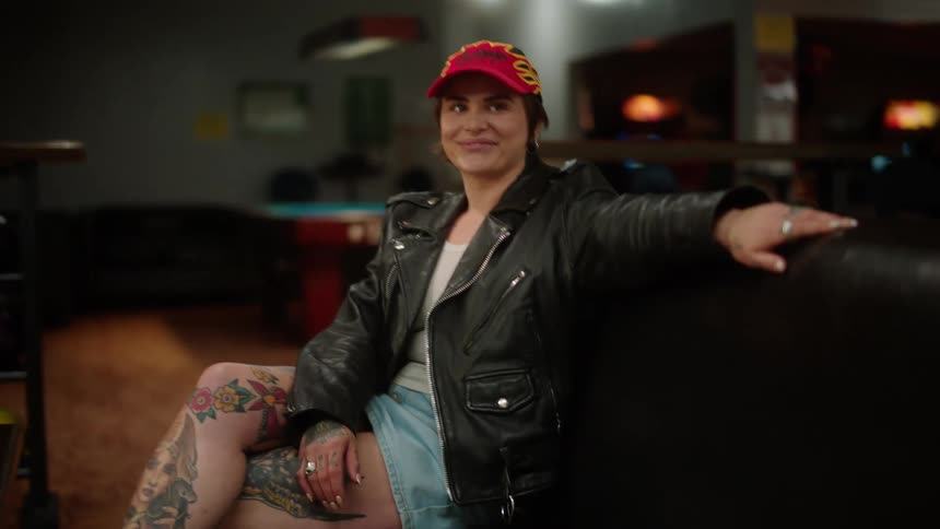 Smiling woman sitting in a black armchair placing a bottle of beer on top of a table