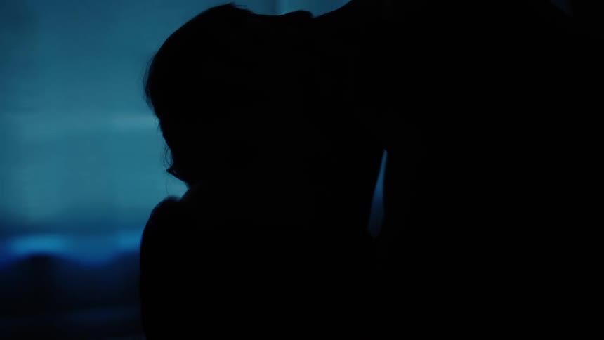 Silhouette of a man and a woman kissing lying in a dark room