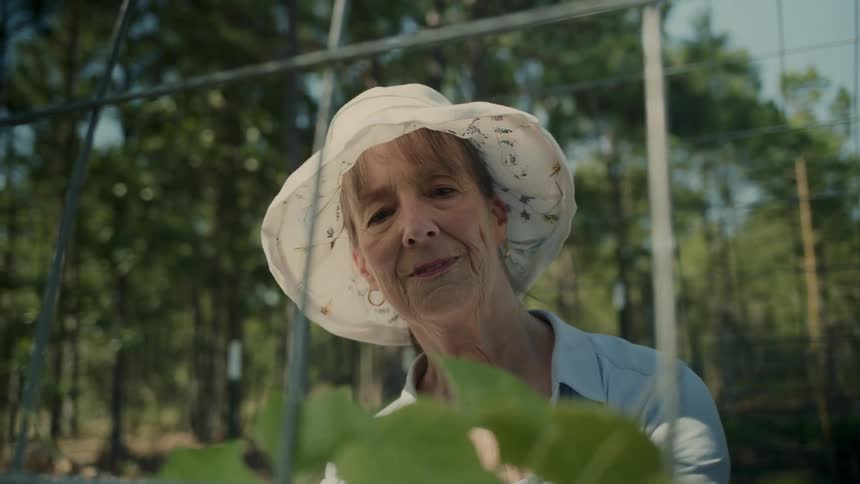 Elderly woman smiling and wearing a white sun hat gardening outdoors