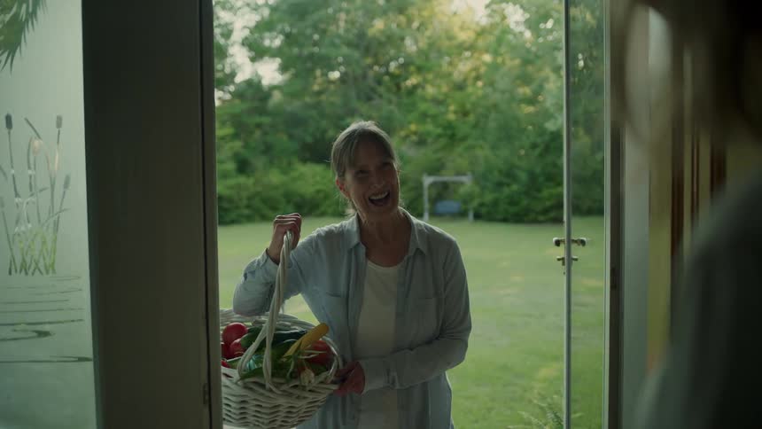 Woman opening the door and a smiling lady talking with a white basket with vegetables