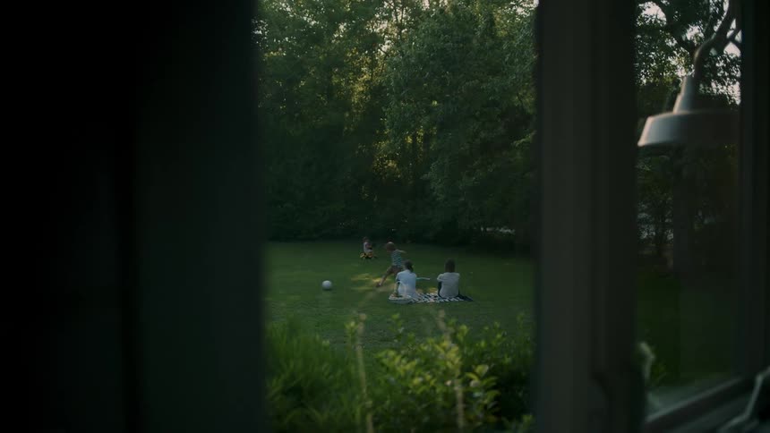 Family in a garden resting and playing seen through a glass window