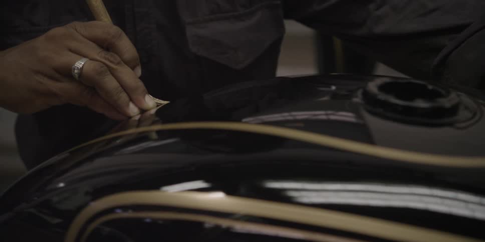 A man paints detail onto a motorcycle tank with a small paintbrush