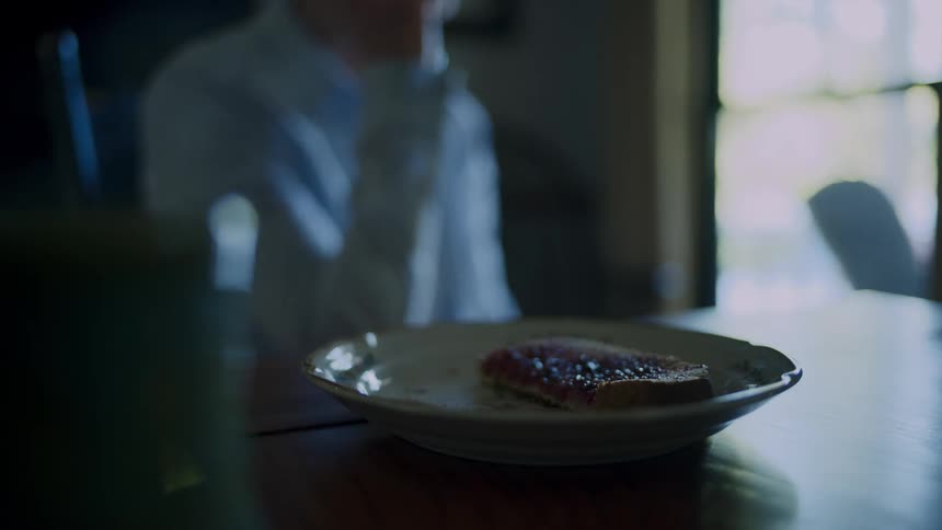 A seated person reaches for a slice of toast with jam and takes a bite