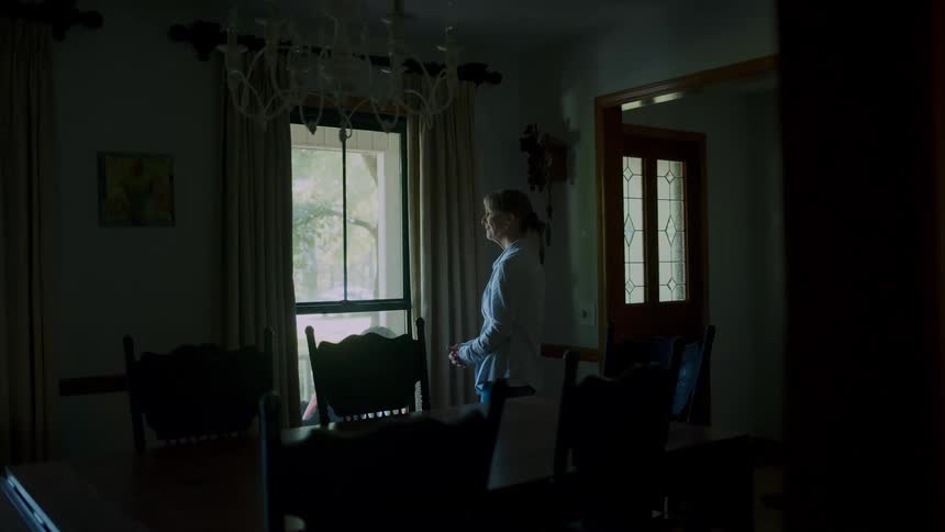 Distressed woman looking out the window from a dark room