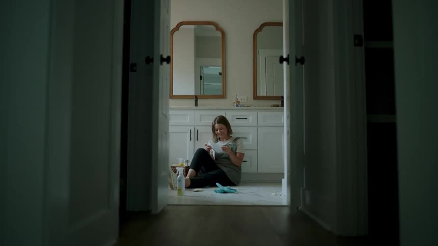 A woman is sitting in the bathroom and reading a letter
