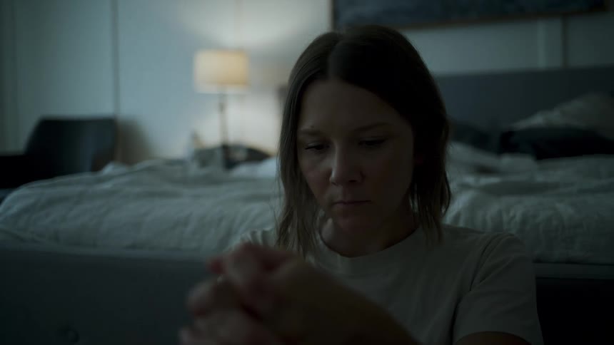 Portrait of a sad woman sitting on the floor next to the bed in a bedroom