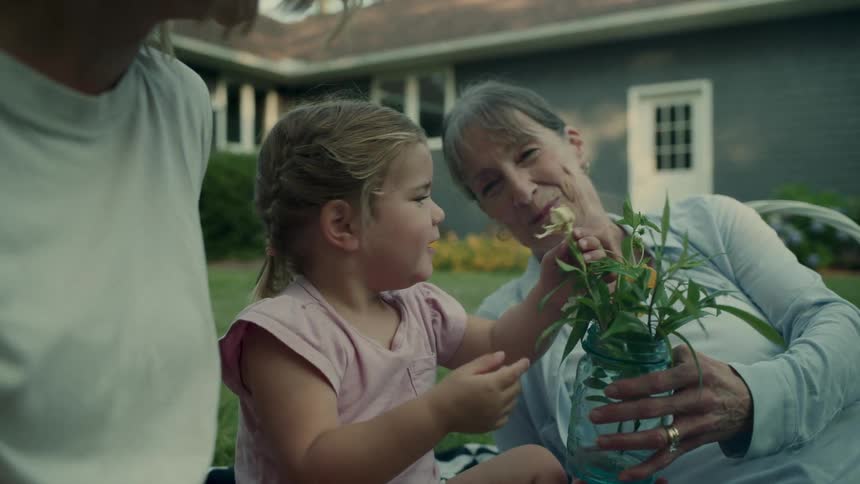 A grandmother and granddaughter enjoying time together arranging flowers in a jar in the backyard
