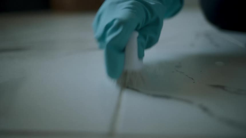 Gloved hand cleaning a white surface with a scrubbing brush