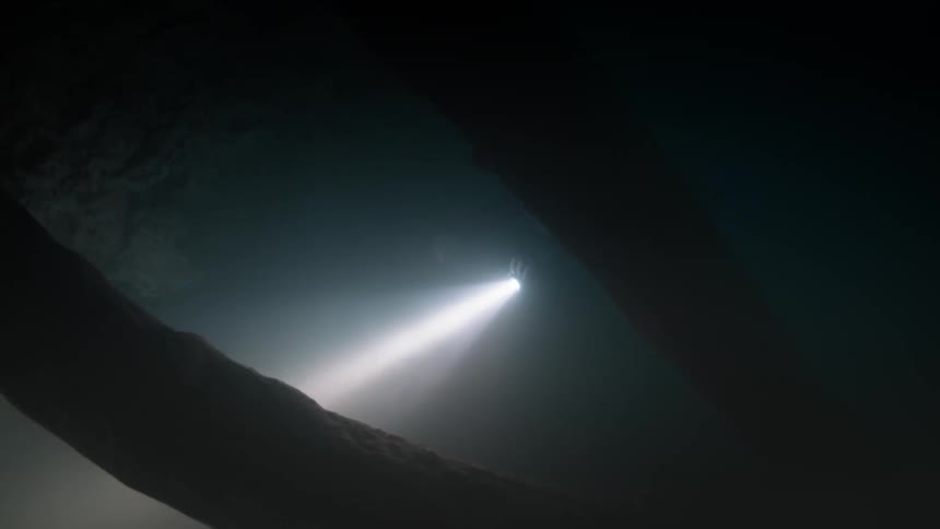 View from inside a dark watery cave with a diver venturing out