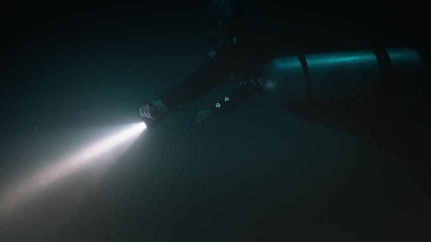 Diver with a flashlight in a dark ocean