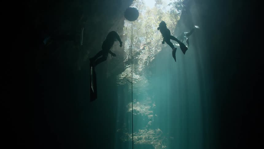 Scuba divers rising to the surface near a buoy in an underwater cave