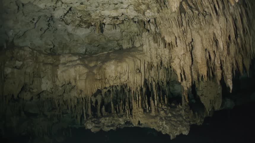A rocky cave has innumerable stalactites hanging down from its ceiling