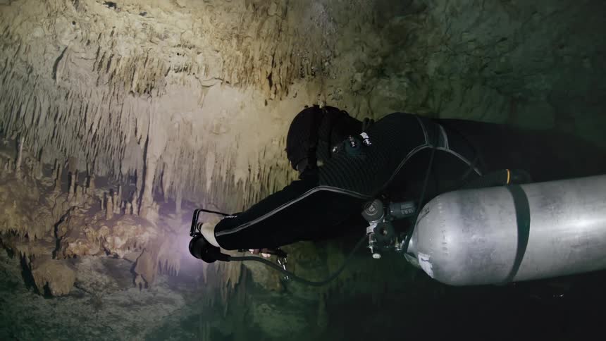 A person in diving equipment is underwater in a dark cave