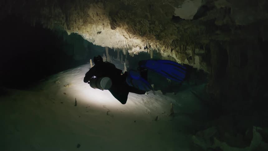 A lone scuba diver explores an underwater cave using a flashlight